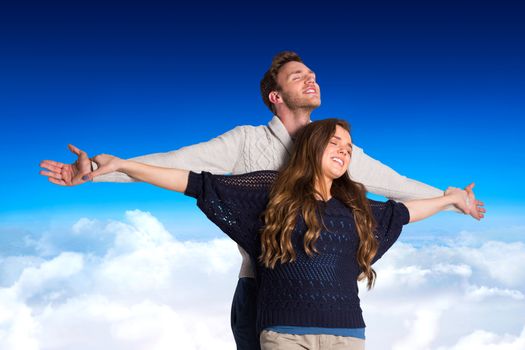 Romantic young couple with arms out against blue sky over clouds