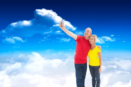 Happy mature couple taking a selfie together against bright blue sky with clouds