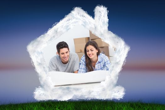 Couple lying on the floor and looking at house plans against green grass under blue and purple sky