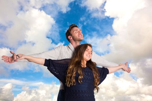 Romantic young couple with arms out against blue sky with white clouds