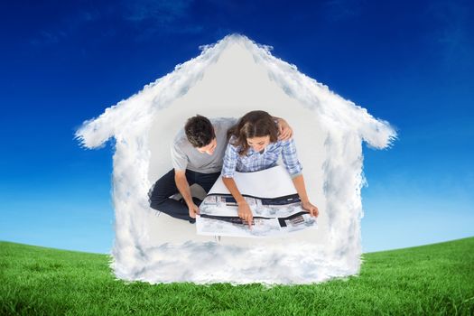 Overview of a husband and his wife looking at house plans against green field under blue sky