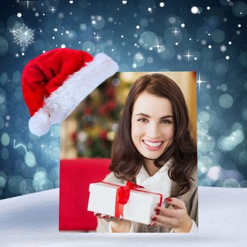 Smiling brunette holding gift on the couch at christmas against blue abstract light spot design
