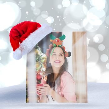 Smiling brunette in christmas hat holding mug against white glowing dots on grey