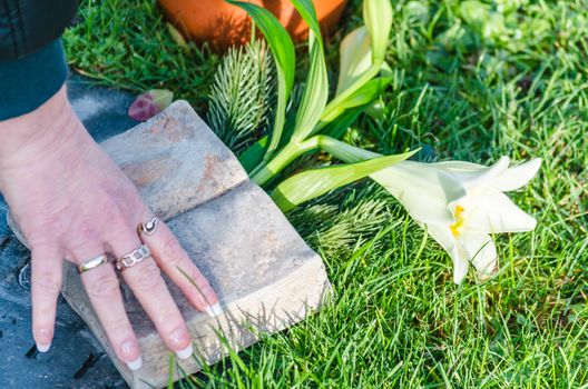 Female hand on a grave stone with flowers.