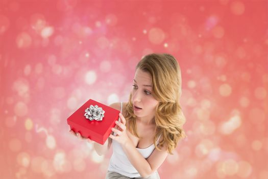 Surprised woman holding a gift against red abstract light spot design