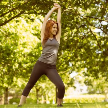 Pretty athletic redhead stretching in park in a sunny day