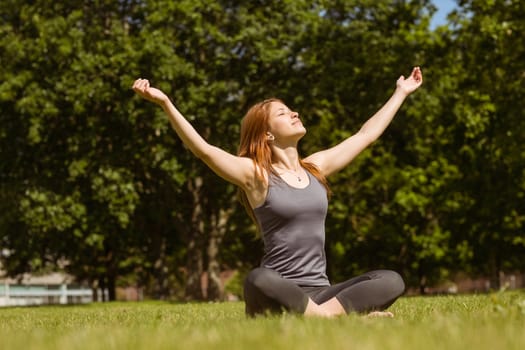 Portrait of a pretty redhead in lotus pose at sunlight