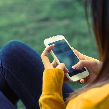 Side view of young woman text messaging in the park