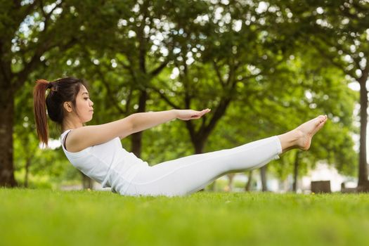 Full length side view of toned young woman doing the boat pose in park