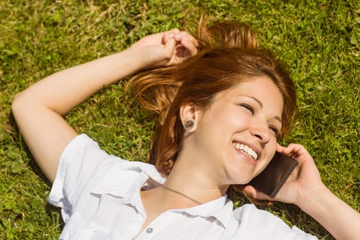 Pretty redhead calling and lying on grass at summer