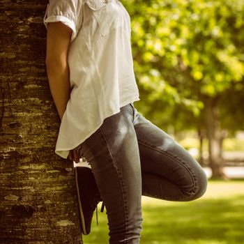 Mid section of a pretty redhead leaning against trunk in park