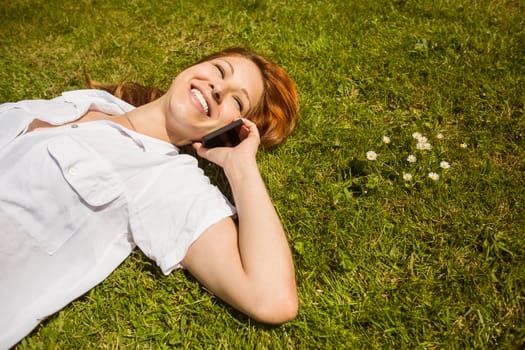 Pretty redhead calling and lying on grass at summer