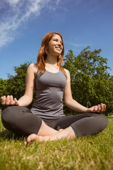 Portrait of a pretty redhead relaxing in lotus pose in park at sunshine