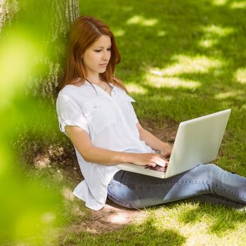 Pretty redhead typing on her laptop in park on a sunny day