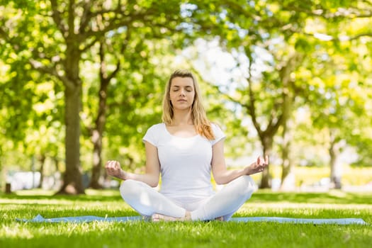 Fit blonde sitting in lotus pose in the park on a sunny day