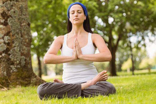 Brunette sitting in lotus pose with hands together on grass in the park