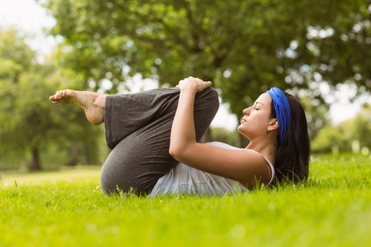 Content brunette doing yoga on grass in the park