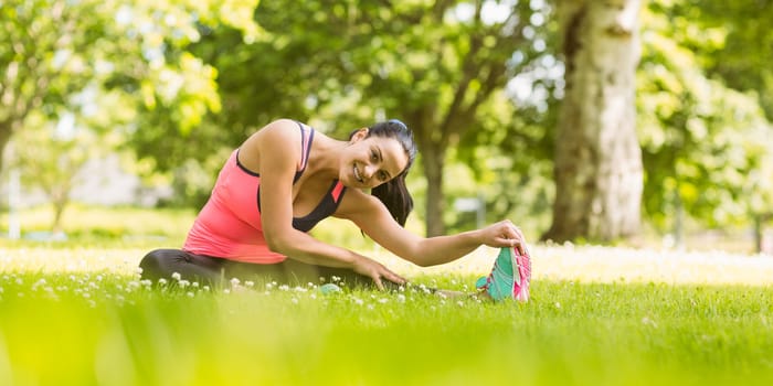 Smiling fit brunette stretching on the grass in the park