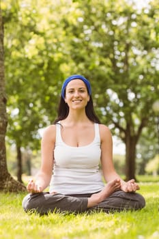 Smiling brunette in lotus pose on grass in the park