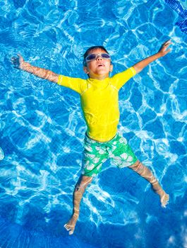 Cute happy little boy in goggles swimming and snorking in the swimming pool