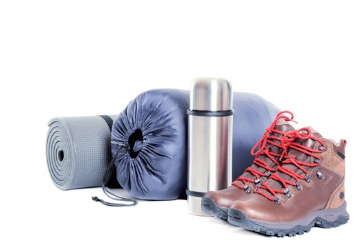 Hiker equipment: pair of mountain boots, thermo flask, sleeping bag and mat on white background