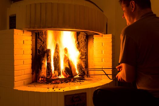 Man adjusting firewood in burning fireplace