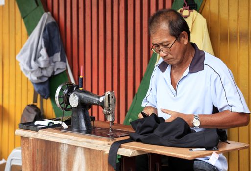 Kota Kinabalu, Malaysia-  December 31, 2014: Street tailor with his old mechanic sewing machine at work in his small shop. This kind of job is very common in Malaysia.