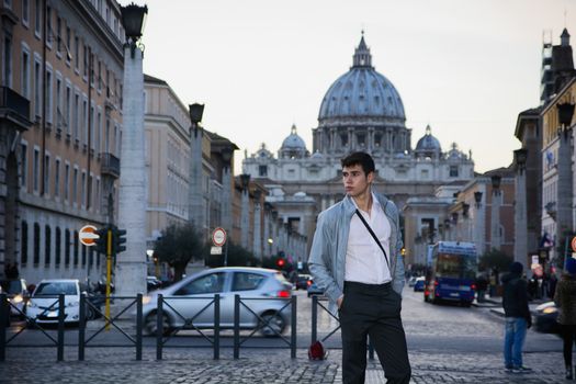 Young man standing in front of St. Peter's Square in Vatican City, with cathedral's dome in the distance