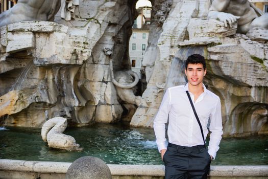 Smiling handsome young man posing in front of fountain in Navona Square, Rome, Italy