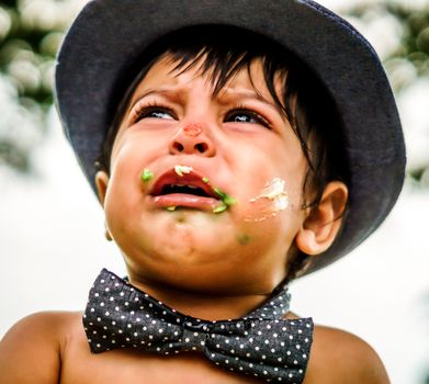Close up outside shot of crying latino baby with cake frosting on his face