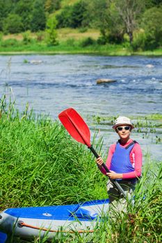 Portrait of happy cute girl holding paddle near a kayak on the river, enjoying a lovely summer day