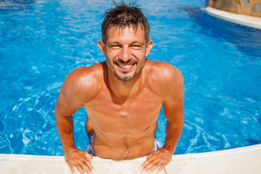 Portrait of a handsome and happy mid aged man relaxing resting on his hands at the side of a swimming pool.