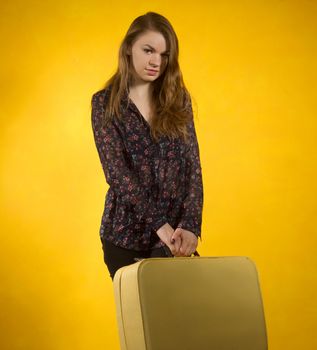 girl with a suitcase on a background of yellow wall