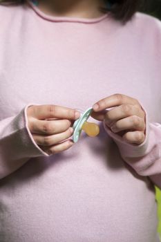 pregnant young woman pink jersey with green pacifier in her hands and green trees background