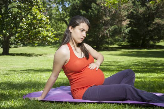 pregnant young woman with orange shirt touching her tummy at a park in Madrid Spain Europe