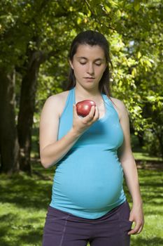 pregnant young woman with orange shirt eating red apple at a park in Madrid Spain Europe