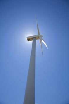 white wind renewable power turbine with sun on top and blue sky background next to Madrid Spain Europe