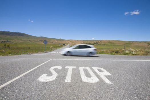 crossroads with stop symbol white painted on asphalt and fast car in rural road next to Madrid Spain Europe