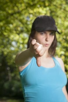 pregnant young woman with blue shirt black cap thumb down over green trees background street