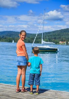 Summer vacation  at the lake - two happy kids walking on the pier and watching on the yacht