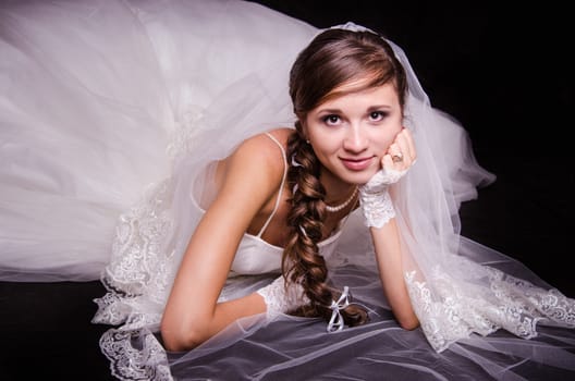 Portrait of the bride of the European type, lying on a black background in a wedding dress
