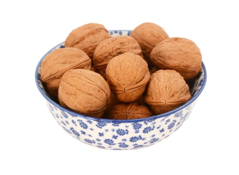 Walnuts in shells, in a blue and white porcelain bowl with a floral design, isolated on a white background