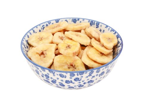 Dried banana chips in a blue and white porcelain bowl with a floral design, isolated on a white background
