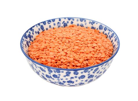 Red lentils in a blue and white porcelain bowl with a floral design, isolated on a white background