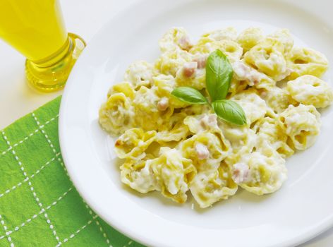 Delicious stuffed pasta tortellini with cream, ham and basil on white dish. Traditional mediterranean cuisine.