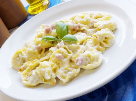 Italian cuisine background. Delicious stuffed pasta tortellini with cream, ham and basil on white dish.