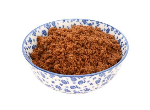 Dark brown soft / muscovado sugar in a blue and white porcelain bowl with a floral design, isolated on a white background