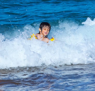 Little boy laughing in the foam of waves at sea on a sunny day