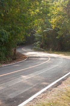 Curvy road down the hill. Road curving down from the mountain. There are more trees on either side of the road.