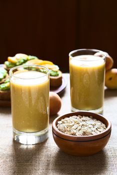 Mango-oatmeal milkshake with a bowl of rolled oats on the side and avocado sandwiches in the back photographed with natural light (Selective Focus, Focus on the front rim of the glass and the front of the oats in the bowl) 